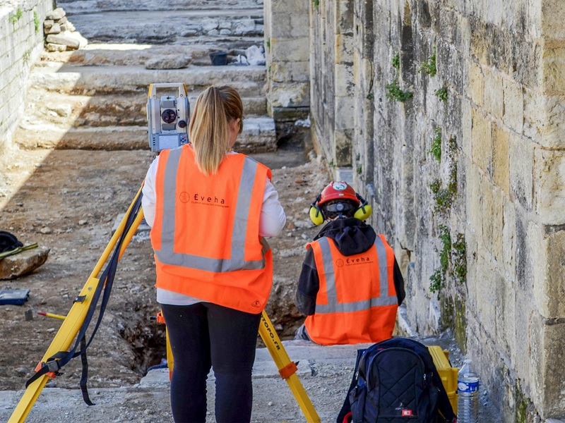 2 jeunes femmes avec un gilet de sécurité prenant des mesures topographiques sur un chantier de fouilles archéologiques